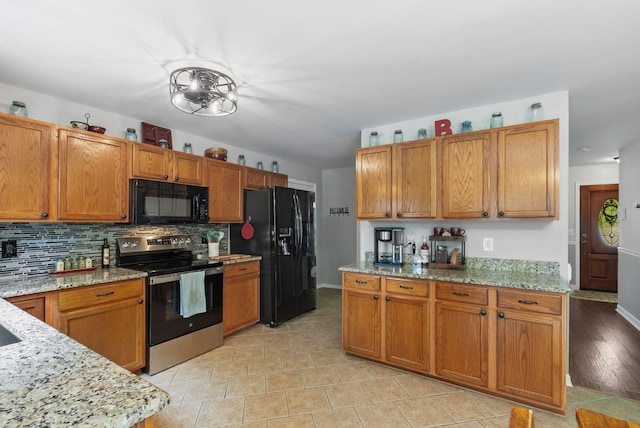 kitchen featuring black appliances, tasteful backsplash, light stone counters, brown cabinets, and baseboards