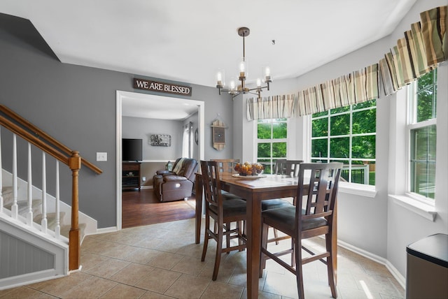 tiled dining room featuring healthy amount of natural light, a chandelier, stairway, and baseboards