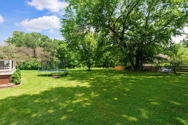 view of yard with a trampoline, a deck, and view of wooded area