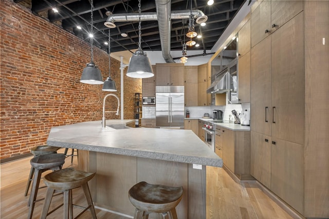 kitchen featuring built in appliances, a sink, brick wall, a high ceiling, and a kitchen breakfast bar