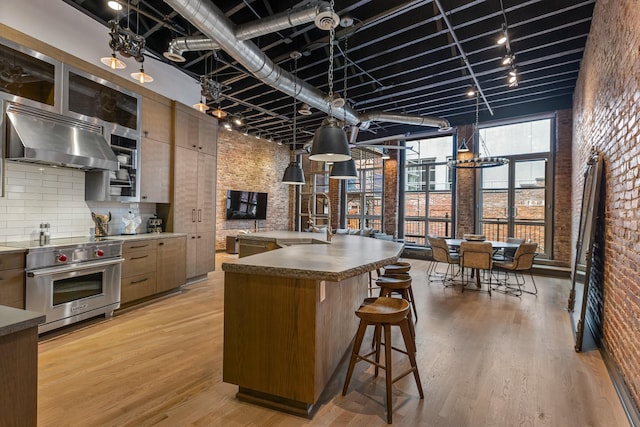 kitchen featuring brick wall, premium range, ventilation hood, light wood-type flooring, and tasteful backsplash