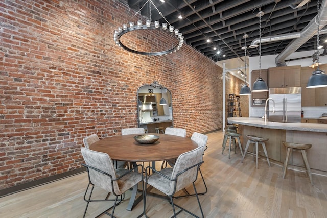 dining area with brick wall, light wood-style floors, and a towering ceiling