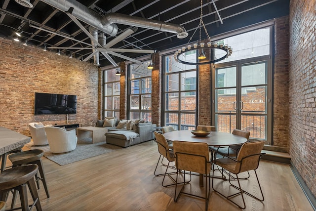 dining space featuring track lighting, a high ceiling, brick wall, a chandelier, and wood finished floors
