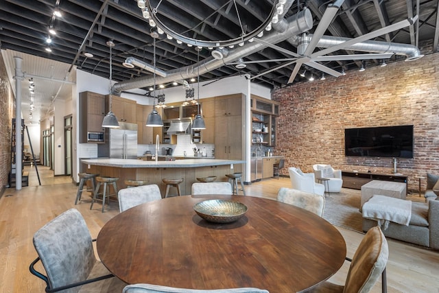 dining room featuring a high ceiling, brick wall, and light wood finished floors
