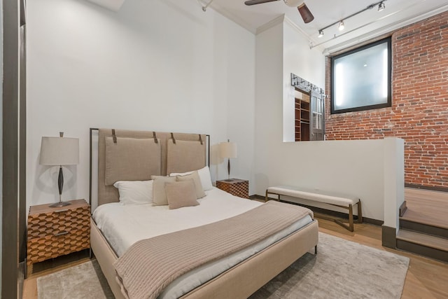 bedroom featuring brick wall, wood finished floors, a ceiling fan, and rail lighting