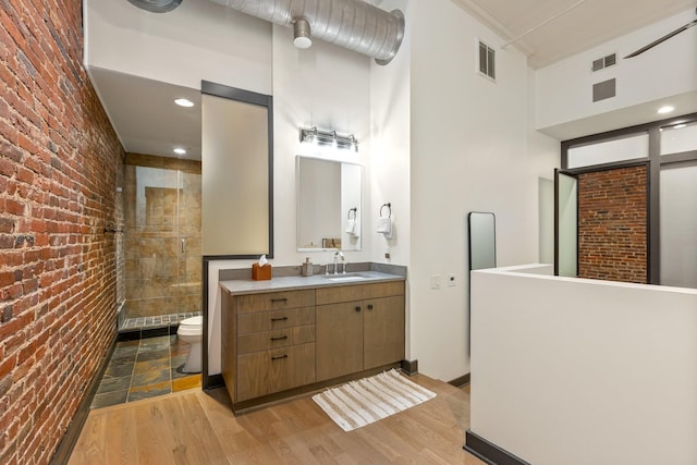 bathroom featuring brick wall, toilet, a tile shower, vanity, and wood finished floors