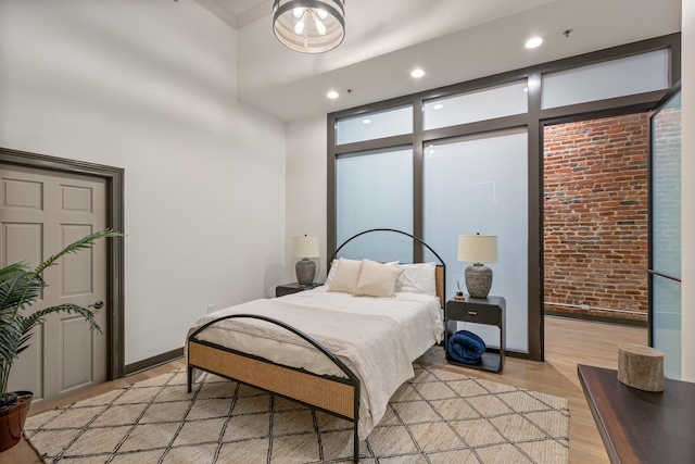 bedroom featuring light wood-type flooring, brick wall, recessed lighting, and baseboards