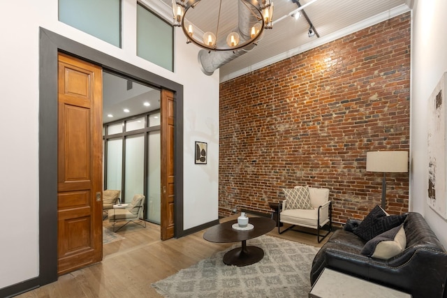sitting room featuring brick wall, wood finished floors, a towering ceiling, track lighting, and baseboards