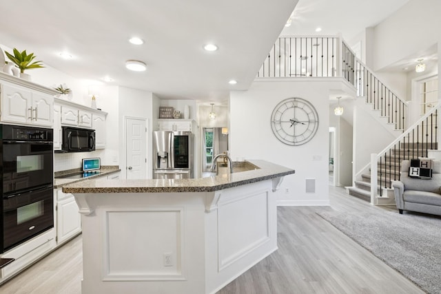 9455 Foothills Ct, Brentwood, TN 37027 - kitchen with black appliances, a kitchen bar, light wood-style flooring, white cabinets, and recessed lighting