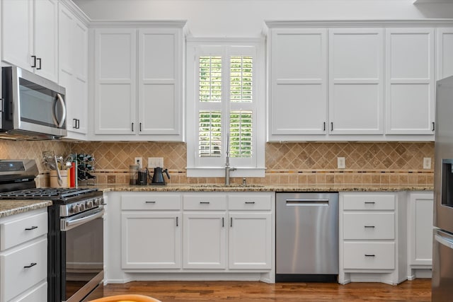 kitchen with stainless steel appliances, white cabinets, light stone countertops, and backsplash