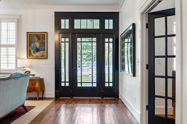 foyer entrance with wood finished floors, baseboards, crown molding, and healthy amount of natural light