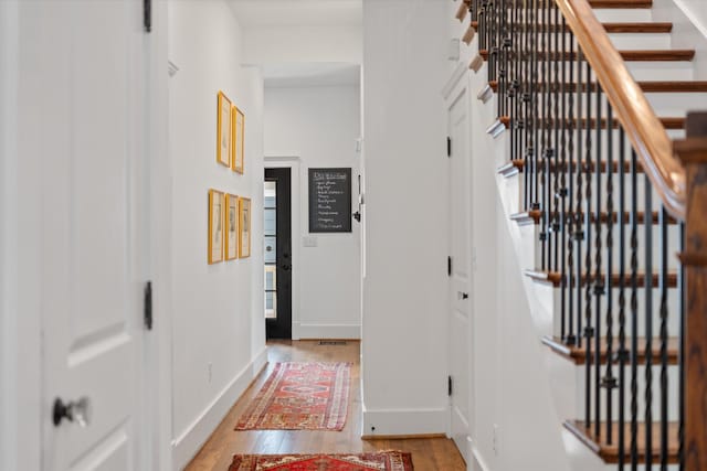 hall with light wood-type flooring, baseboards, and stairs