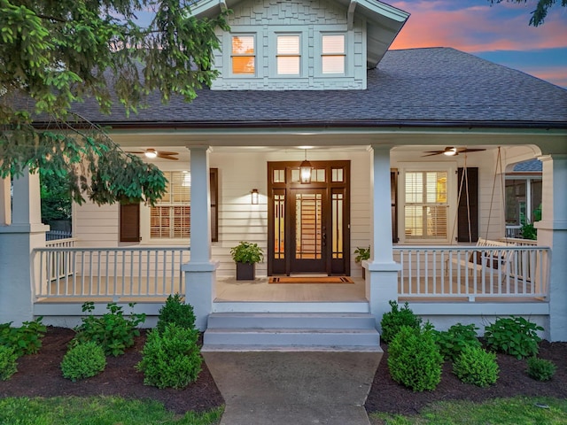 exterior entry at dusk with covered porch, ceiling fan, and roof with shingles