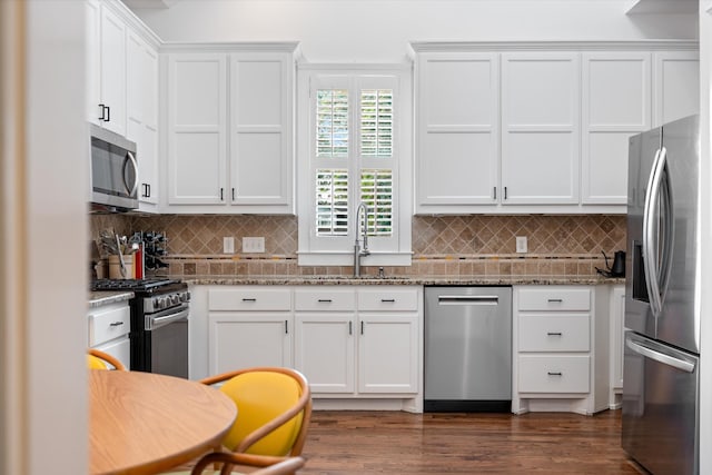 kitchen featuring appliances with stainless steel finishes, a sink, stone countertops, white cabinets, and backsplash