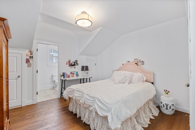 bedroom with wood finished floors, lofted ceiling, baseboards, and ensuite bath