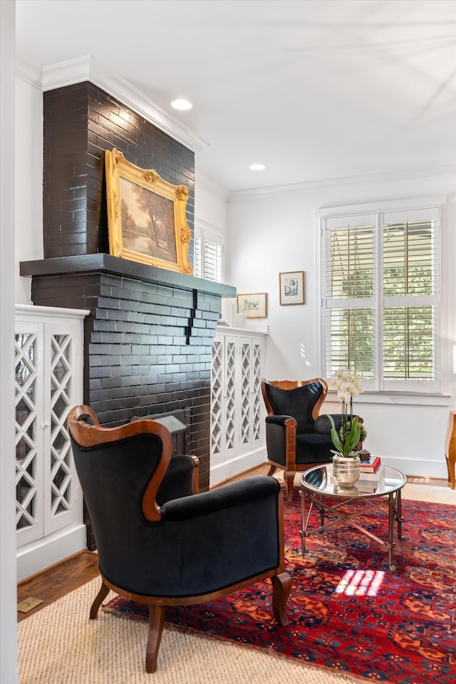 living area with ornamental molding, wood finished floors, a brick fireplace, and baseboards