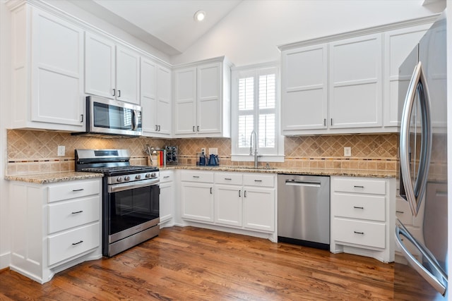 kitchen with appliances with stainless steel finishes, a sink, vaulted ceiling, white cabinetry, and recessed lighting