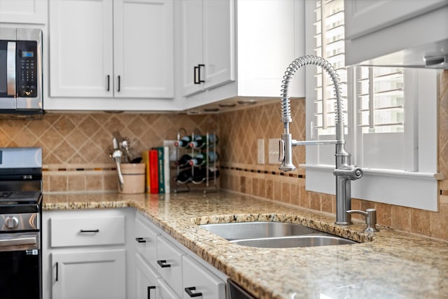 kitchen with a sink, appliances with stainless steel finishes, white cabinetry, tasteful backsplash, and light stone countertops