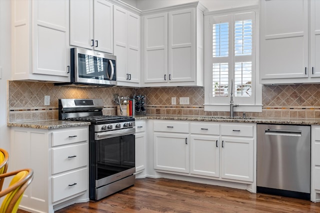 kitchen featuring appliances with stainless steel finishes, a sink, white cabinetry, decorative backsplash, and dark wood finished floors