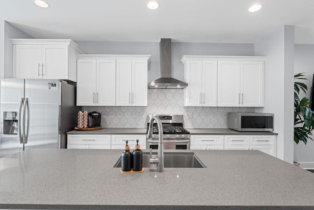 kitchen with wall chimney exhaust hood, stainless steel appliances, a large island with sink, white cabinets, and recessed lighting