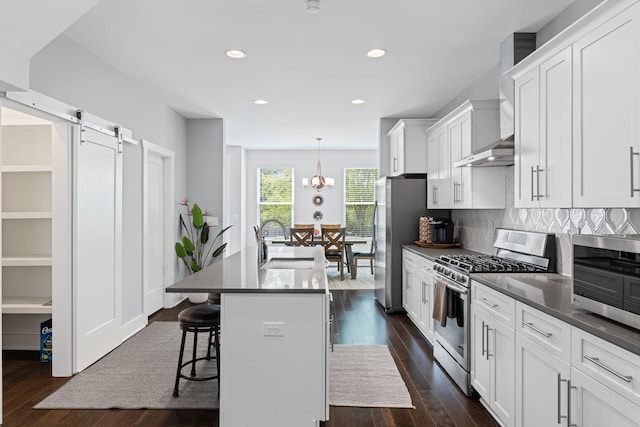 kitchen featuring appliances with stainless steel finishes, a center island with sink, dark wood-style floors, a kitchen breakfast bar, and dark countertops