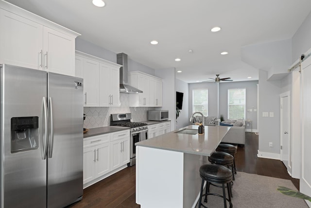 kitchen featuring appliances with stainless steel finishes, a sink, wall chimney range hood, dark wood-style flooring, and recessed lighting