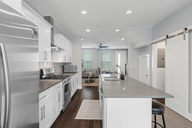 kitchen with appliances with stainless steel finishes, a sink, ceiling fan, a center island with sink, and white cabinetry