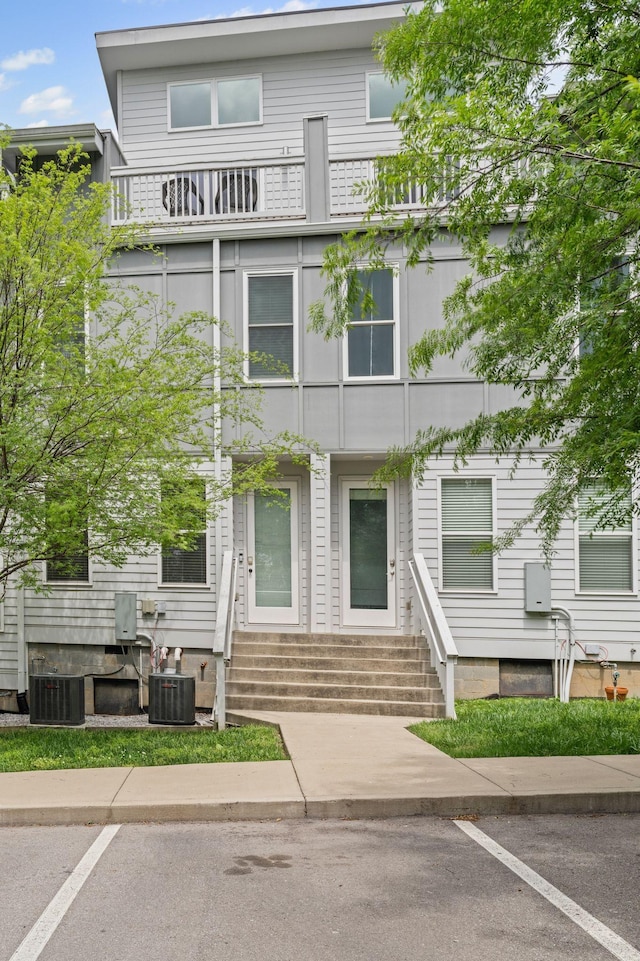 view of front facade with a balcony, central AC, entry steps, and uncovered parking