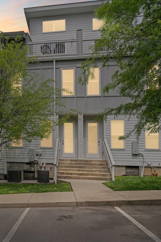 property at dusk featuring entry steps, cooling unit, and uncovered parking