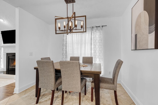 dining room with a chandelier, a warm lit fireplace, and baseboards