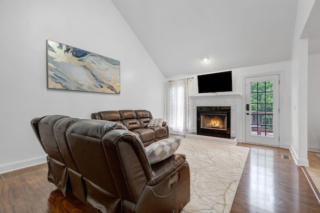 living area with a fireplace, baseboards, wood finished floors, and high vaulted ceiling