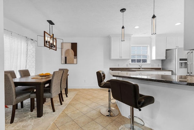 kitchen featuring stainless steel fridge, light tile patterned flooring, white cabinetry, a chandelier, and a kitchen breakfast bar