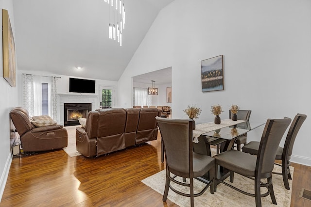dining room featuring a lit fireplace, wood finished floors, high vaulted ceiling, baseboards, and a chandelier