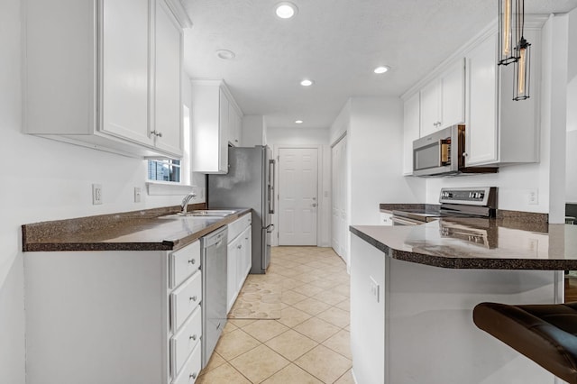 kitchen with appliances with stainless steel finishes, dark countertops, a sink, a peninsula, and white cabinets