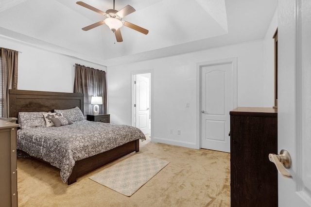 bedroom featuring light carpet, a tray ceiling, baseboards, a ceiling fan, and ensuite bathroom