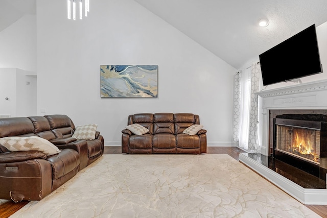 living room featuring a lit fireplace, wood finished floors, high vaulted ceiling, and baseboards