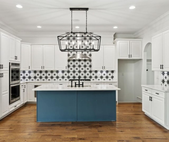 kitchen with double oven, white cabinetry, a center island, a chandelier, and decorative backsplash