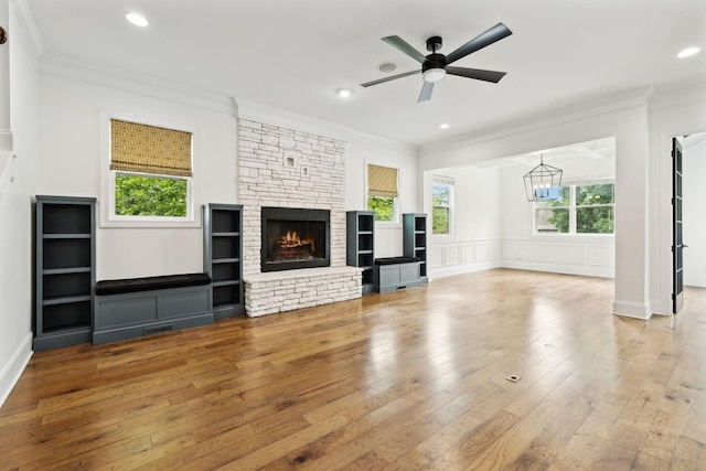 unfurnished living room with ornamental molding, plenty of natural light, hardwood / wood-style floors, a stone fireplace, and a chandelier