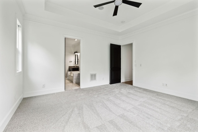 unfurnished bedroom with crown molding, carpet floors, a tray ceiling, ensuite bathroom, and baseboards