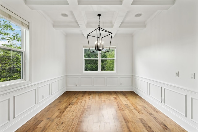 unfurnished dining area featuring healthy amount of natural light, a chandelier, beamed ceiling, coffered ceiling, and light wood-style flooring