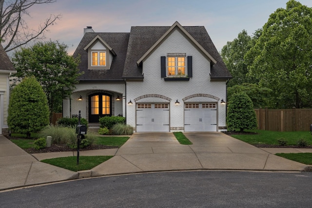 french country inspired facade featuring a garage, concrete driveway, a chimney, fence, and a shingled roof