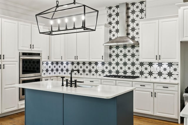 kitchen featuring wall chimney exhaust hood, appliances with stainless steel finishes, light countertops, a sink, and white cabinets
