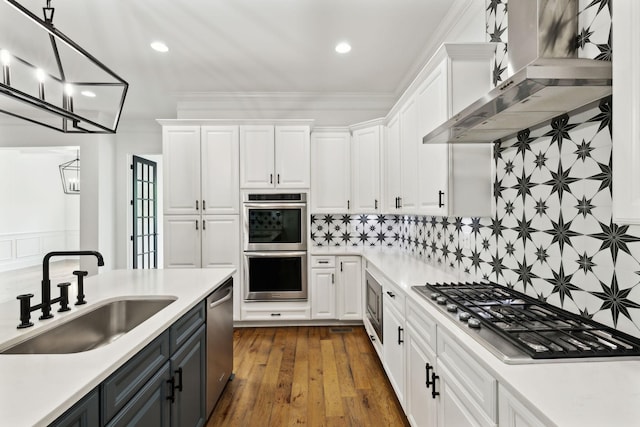 kitchen with a sink, appliances with stainless steel finishes, wall chimney exhaust hood, white cabinets, and recessed lighting