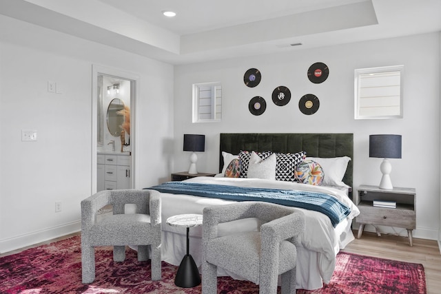 bedroom with baseboards, wood finished floors, a tray ceiling, connected bathroom, and recessed lighting