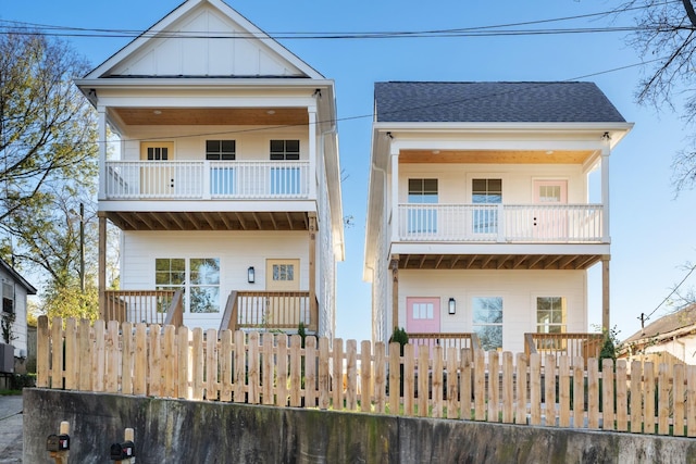 view of front of home featuring a balcony, a fenced front yard, board and batten siding, and a shingled roof