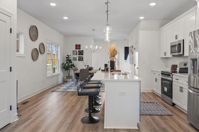 kitchen with stainless steel appliances, a sink, an island with sink, a breakfast bar, and light wood-type flooring