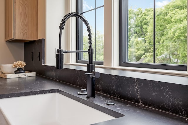 kitchen view of dark countertops, a sink, brown cabinets, and backsplash