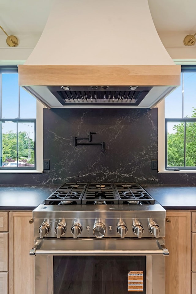 kitchen with high end stainless steel range, island range hood, dark countertops, and light brown cabinetry