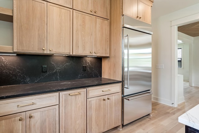 kitchen featuring built in fridge, light brown cabinets, dark stone countertops, tasteful backsplash, and light wood-style flooring
