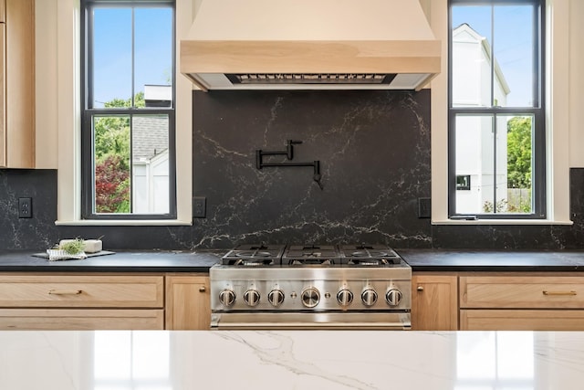kitchen with range, extractor fan, light brown cabinetry, dark countertops, and backsplash